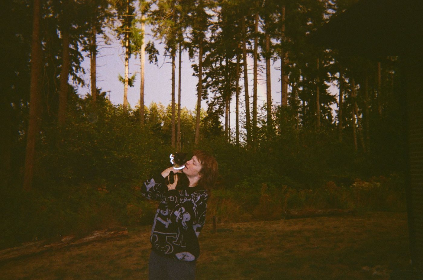 Diane holding Campari up to her face in front of tall evergreen trees at dusk